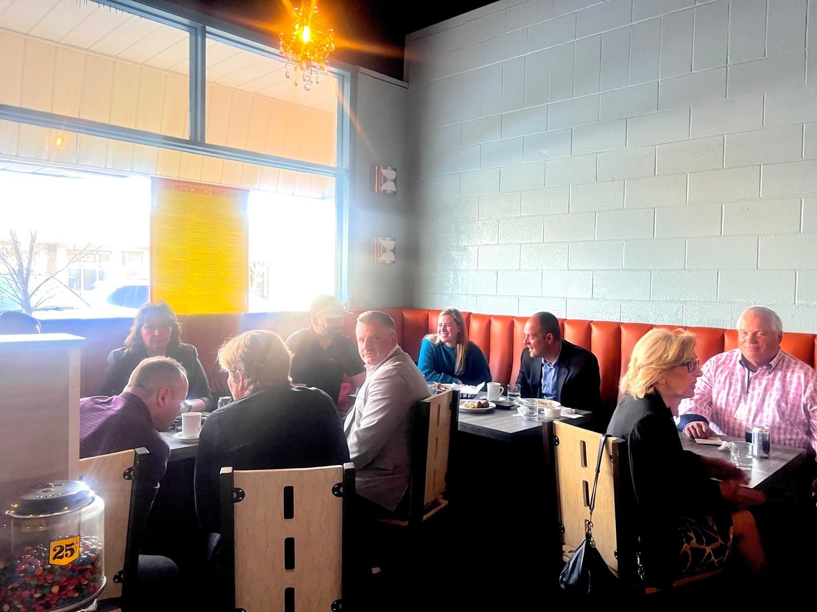 Group of people sitting around a table in a brightly lit restaurant with red seating and large windows.