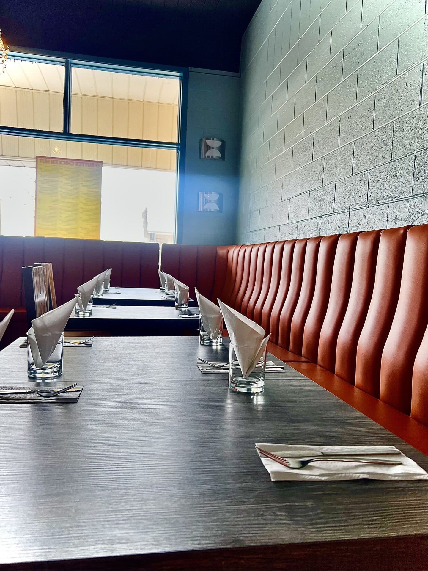 Restaurant interior with neatly set tables, napkins, and brown leather booth seating.